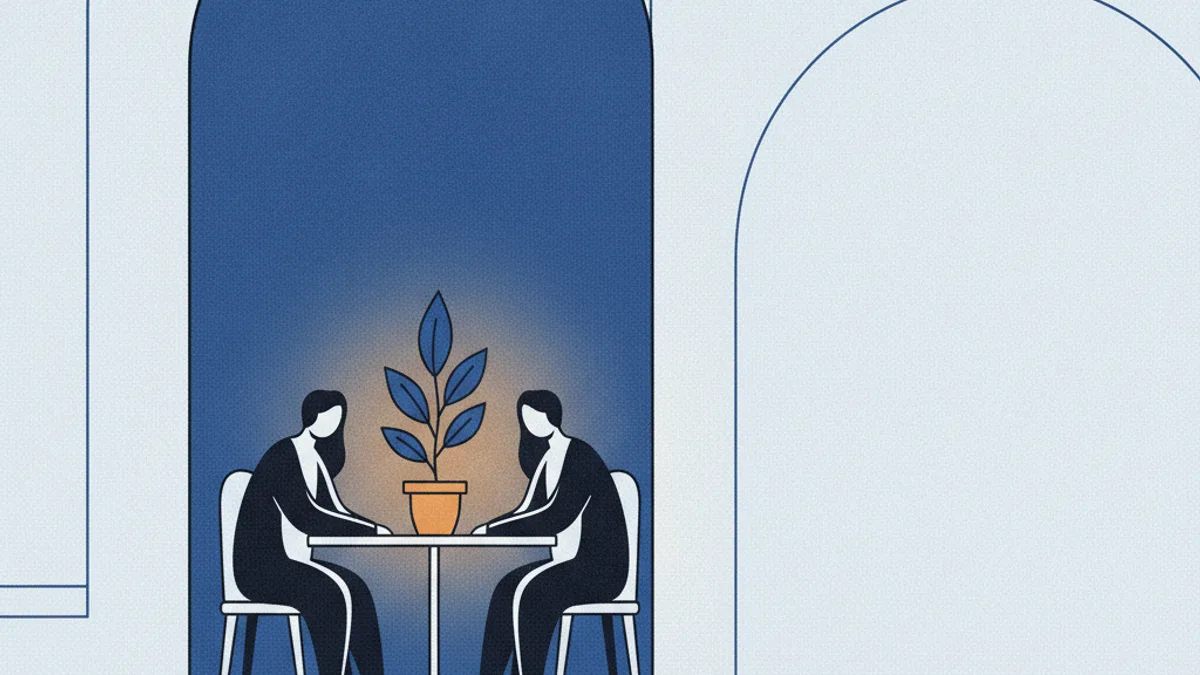 Two people talking at a small table in a quiet corner of an otherwise empty room.